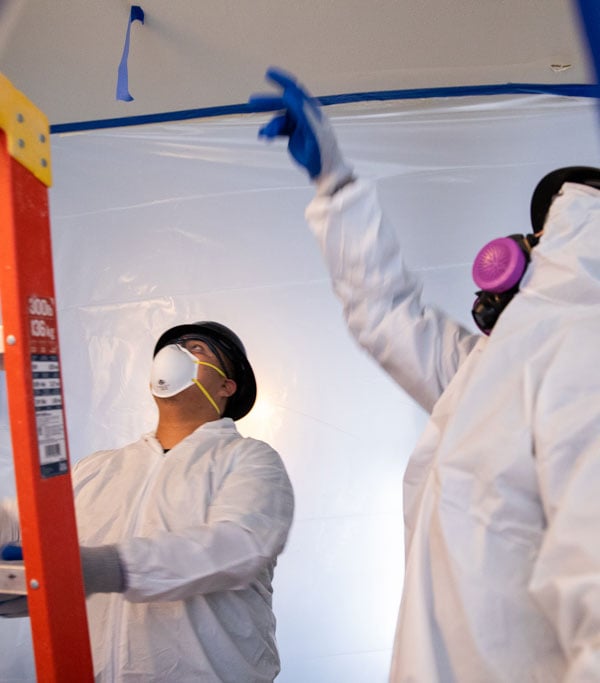 Two workers in Tyvek suits looking at removing mold