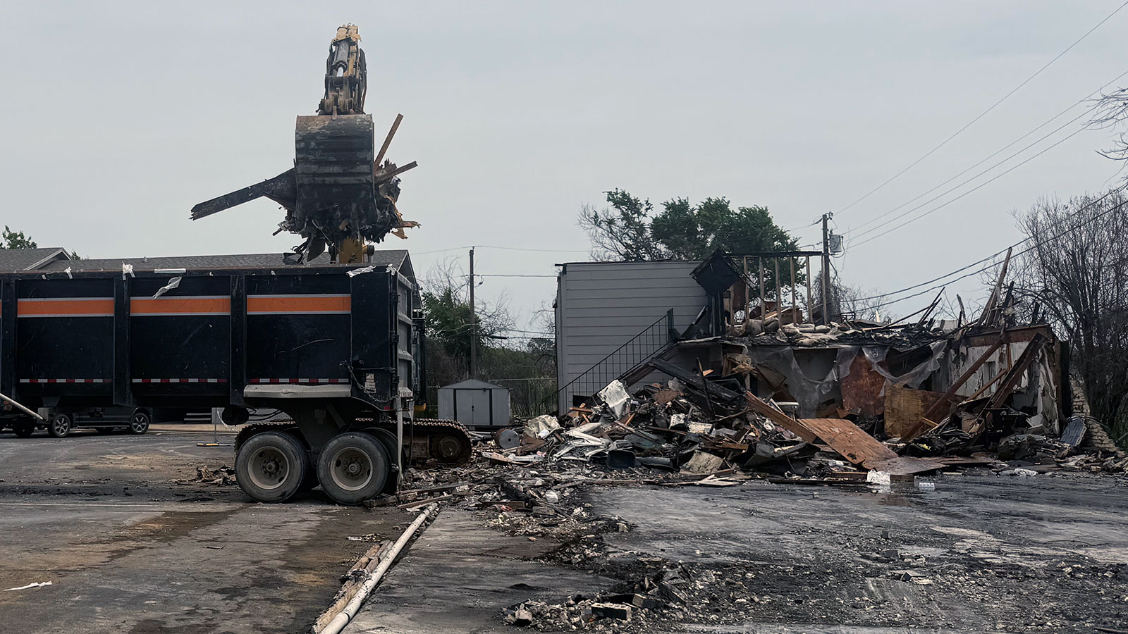 Bucket loader clearing debris from a fire-damaged apartment building demolition in Dallas-Fort Worth.