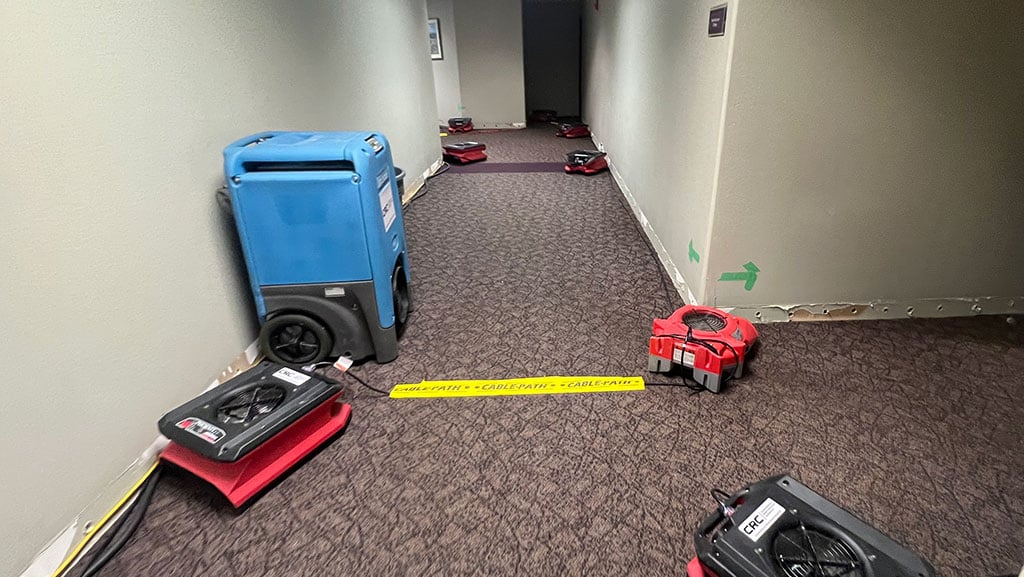 Drying equipment set up in a hallway after water damage from burst pipes, with baseboards removed