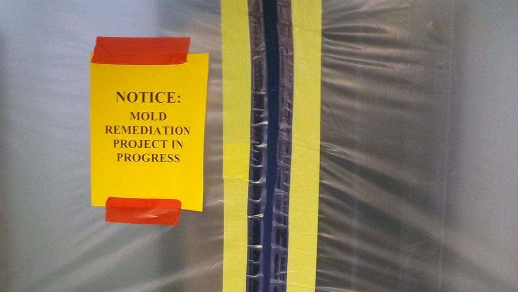 Sign state mold remediation in progress posted on a containment entrance.